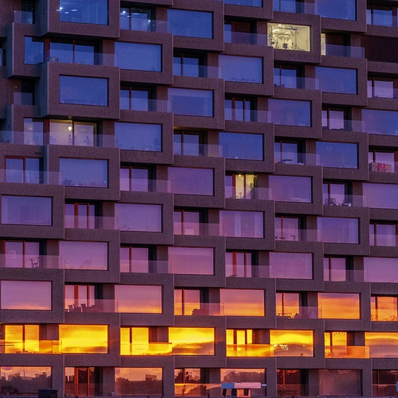 A building's facade, lit up in yellow, orange, purple and blue, possibly reflecting the sunset.